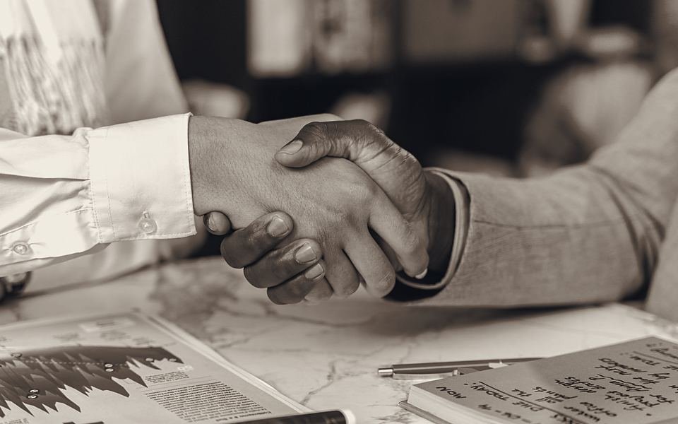 Two people shaking hands over sales charts